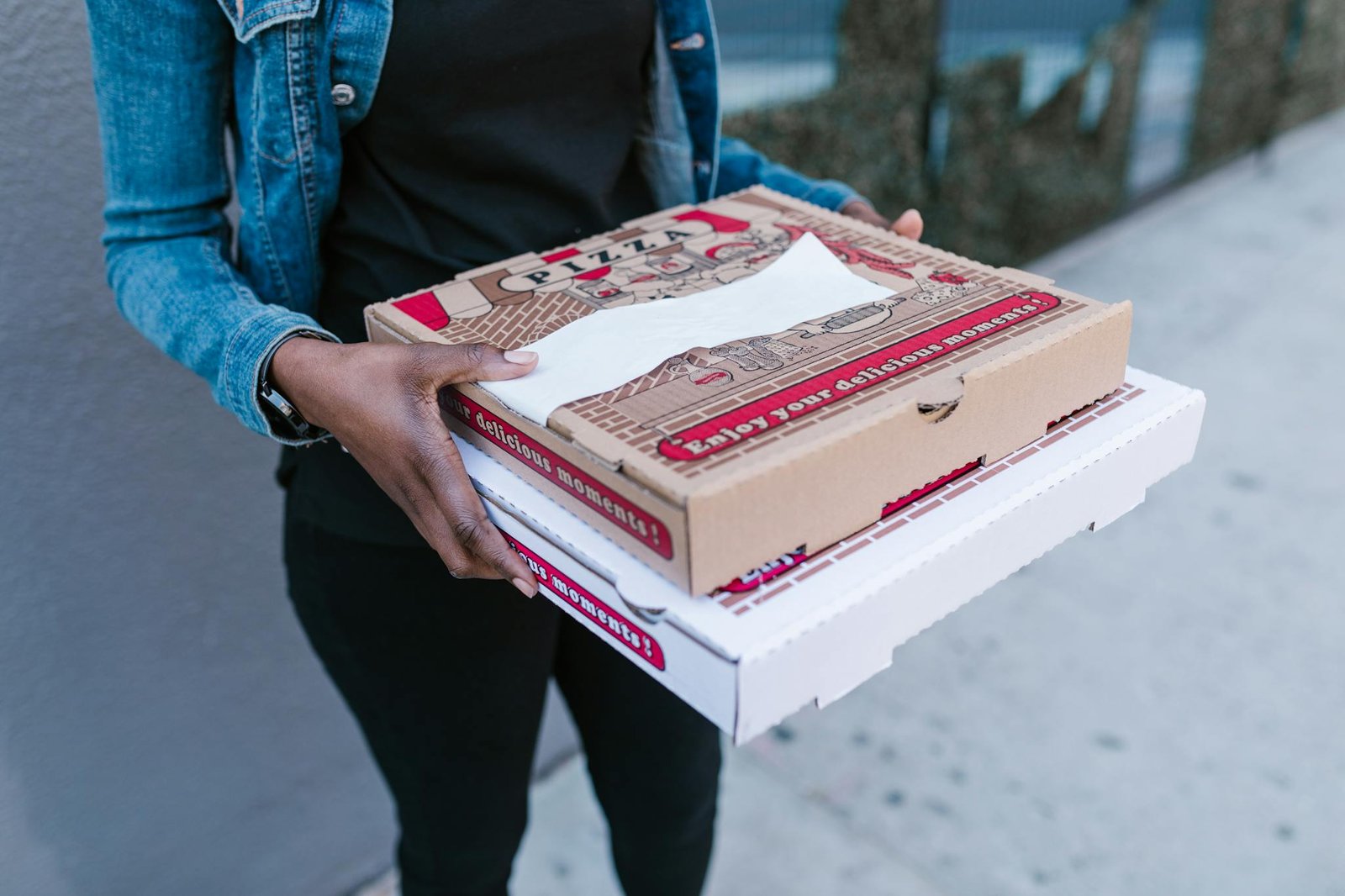 Woman holding pizza boxes for delivery in denim jacket outdoors.